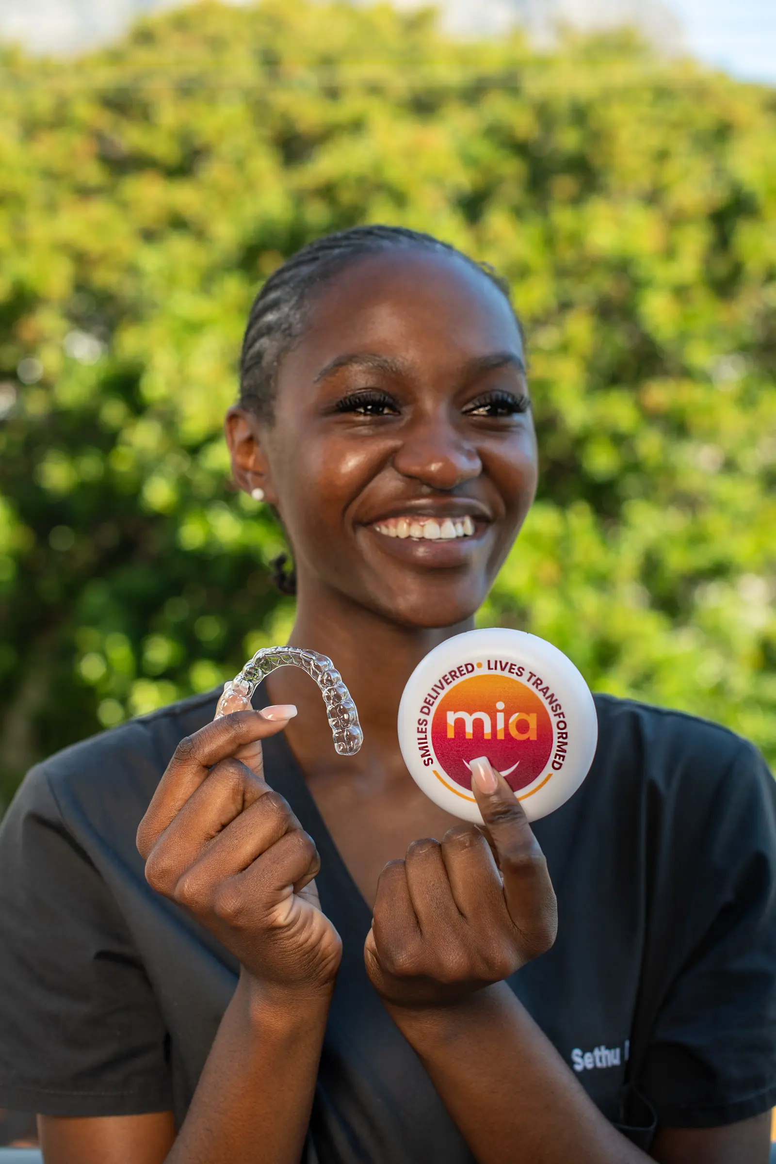 A smiling young woman holding her clear aligner and Mia case